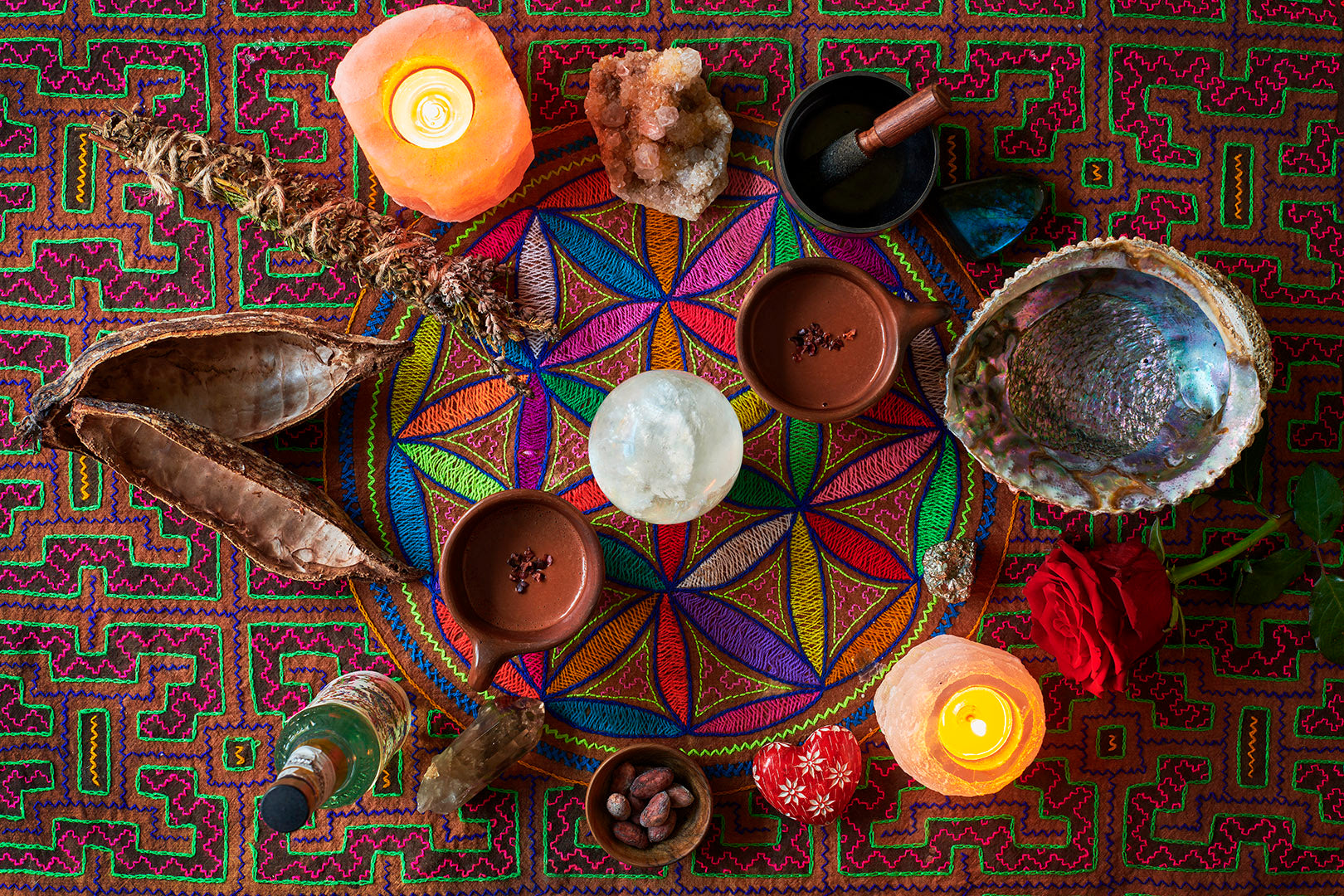 Ceremonial grade cacao from the Peruvian Andes in a handmade ceramic mugs surrounded by altar items for a cacao ceremony, rose, candles and crystals on a shamanic cloth.