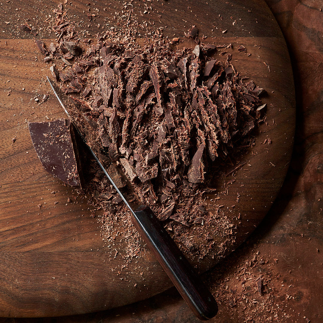 Ceremonial grade cacao from the Peruvian Andes being chopped up on a wooden board on a dark wooden table.