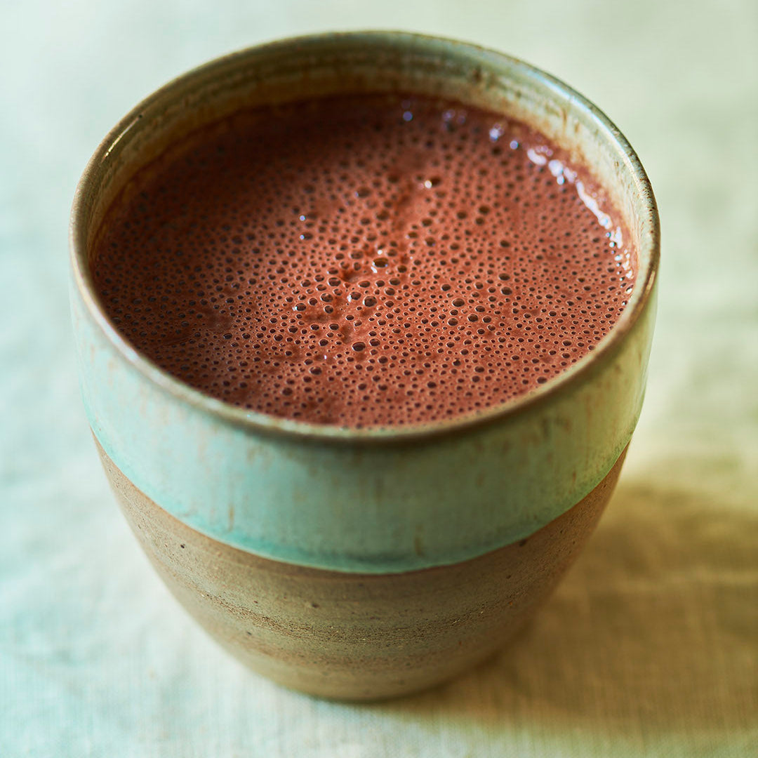 Cup of ceremonial grade cacao from the Peruvian Andes.  In a ceramic green mug on yellow brushed cotton table cloth.